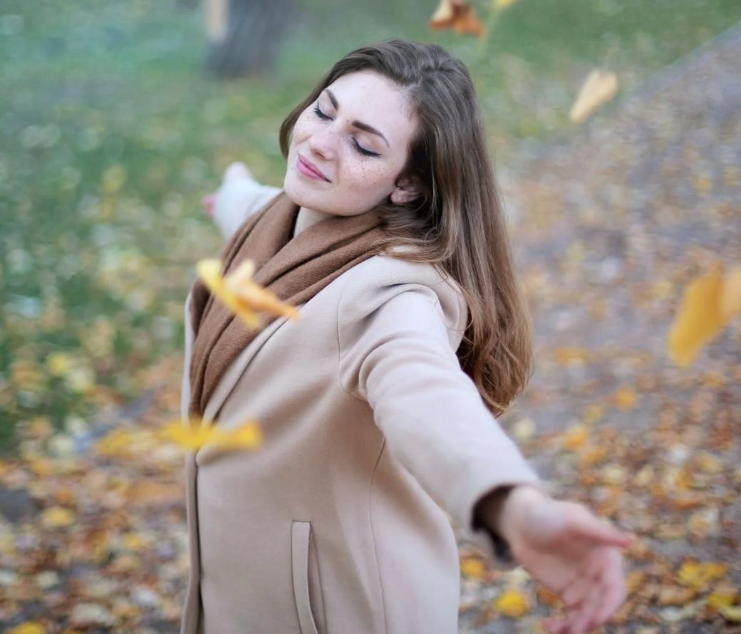 woman feeling happy while leaves falling from tree