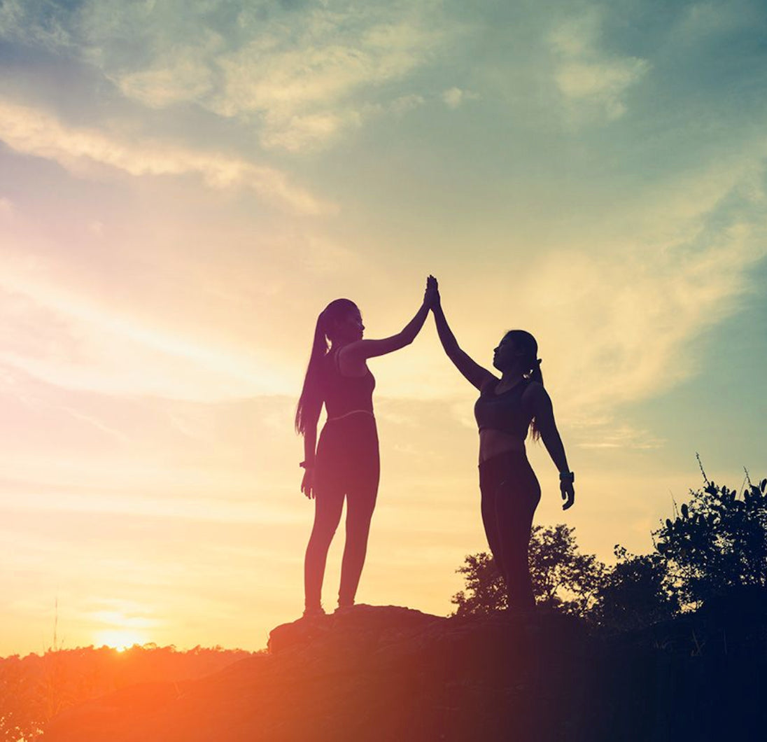 two woman high five each other in the sunset